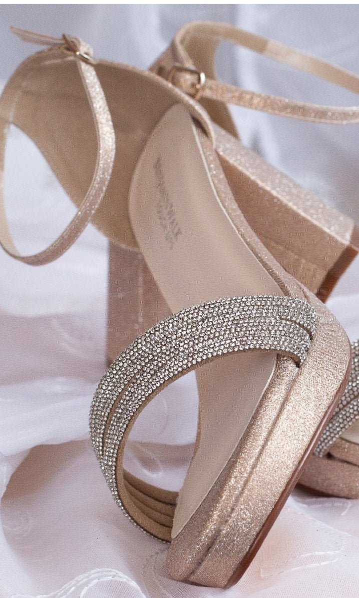 A close-up of Parker Champagne Glitter Prom Shoes: Touch Ups 4659, showcasing rhinestone-encrusted open-toe straps and a low heel, displayed on sheer white fabric.